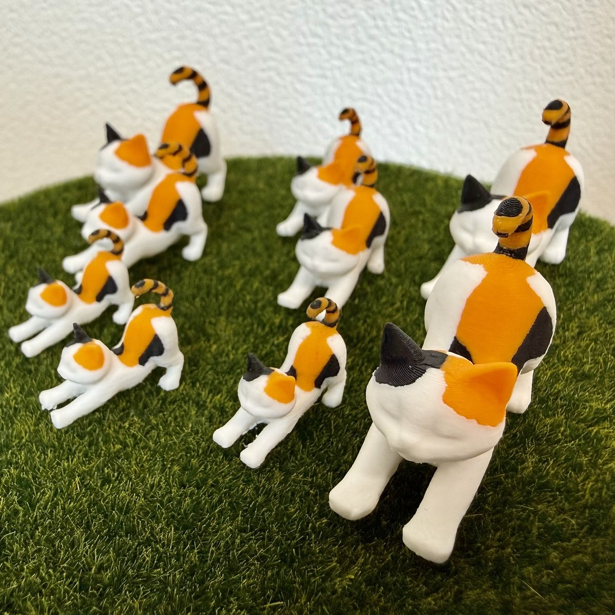 伸びをする三毛猫のミニチュアの群れが、そろっておしりを向けて並んでいるところ